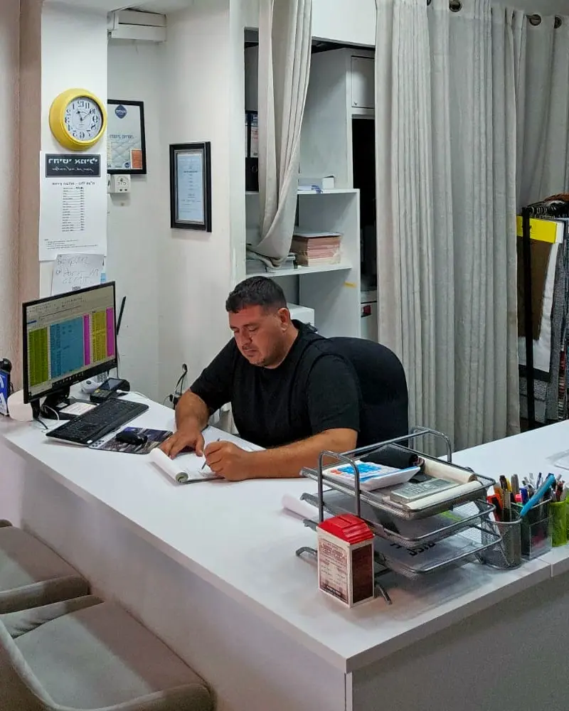 ניסים סעדה, בעל רהיטי אמילי, יושב ליד דלפק הקבלה בחנות בעפולה ורושם הזמנה
